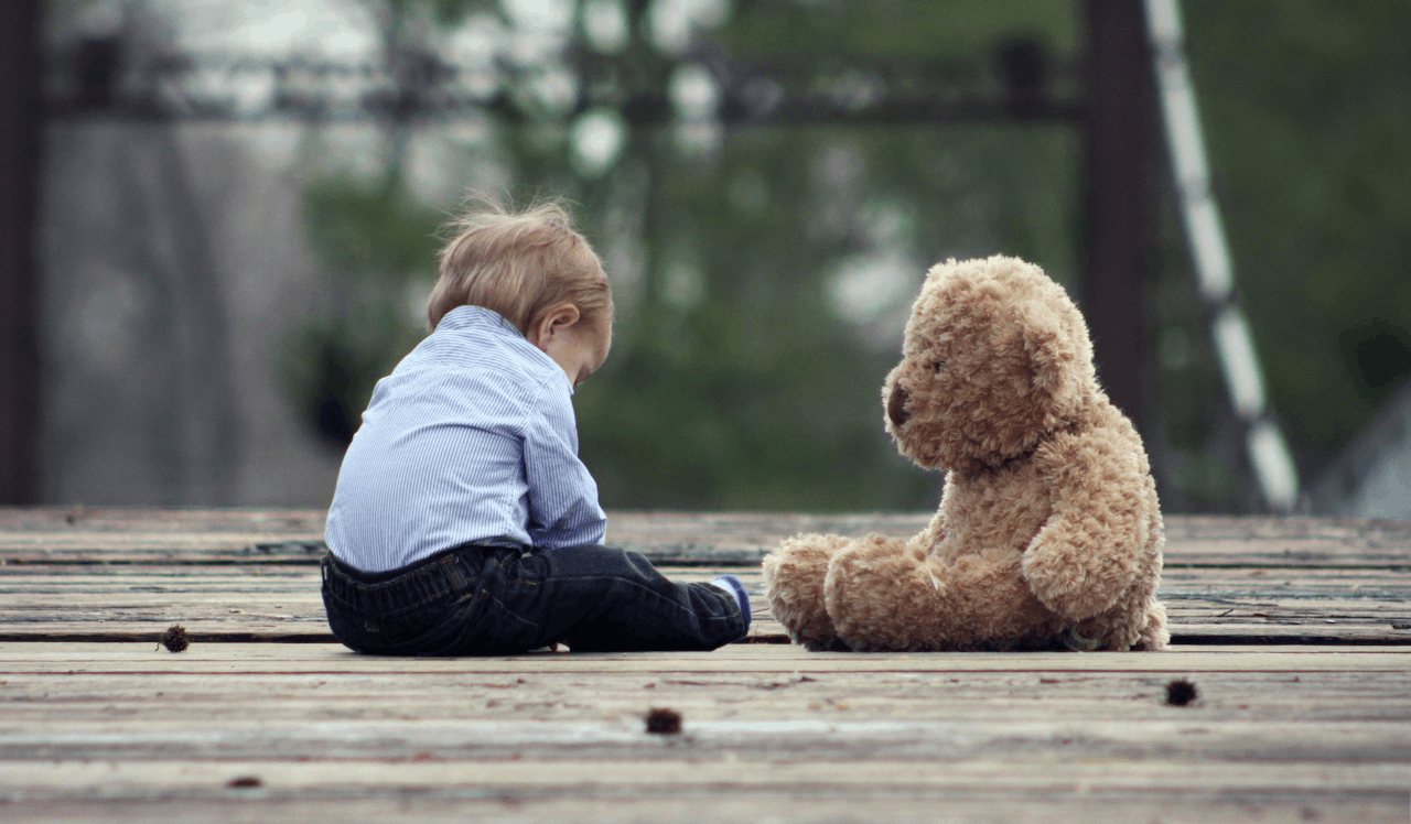 Een kind zit op de grond naast een teddybeer.