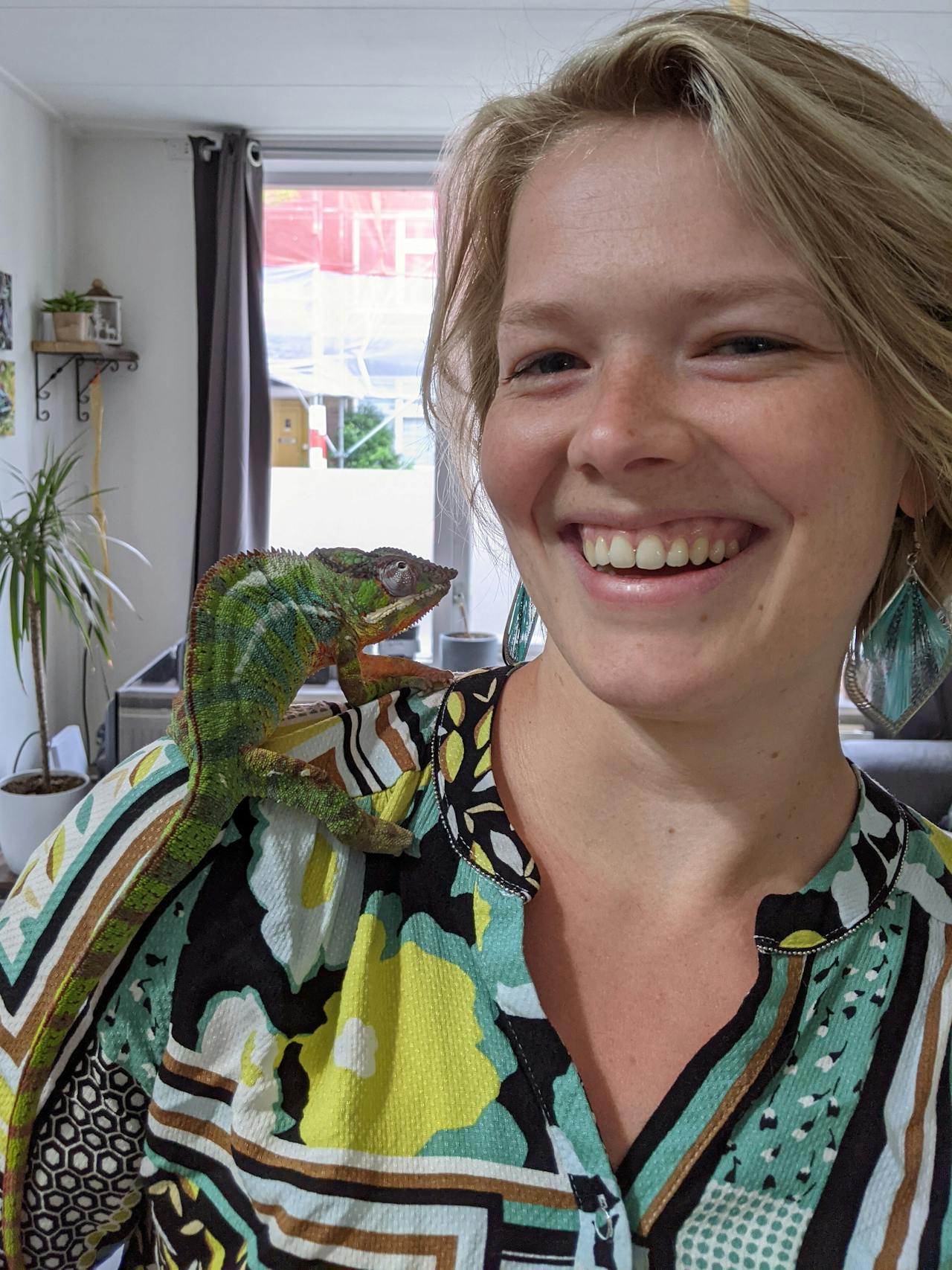 Een vrouw lacht terwijl ze een kameleon op haar schouder heeft.