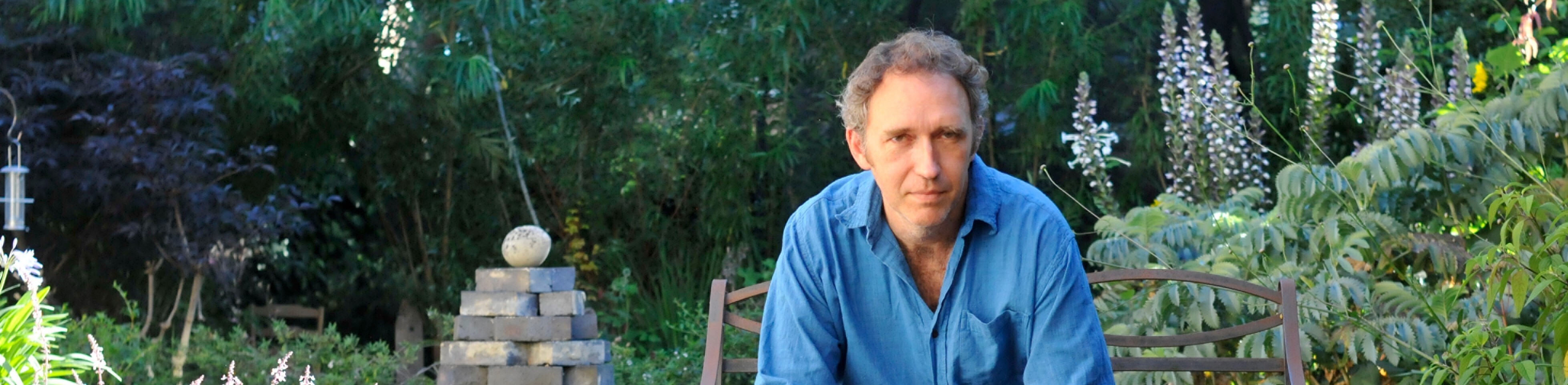 Een man in een blauw shirt zit op een stoel voor een stapel stenen.