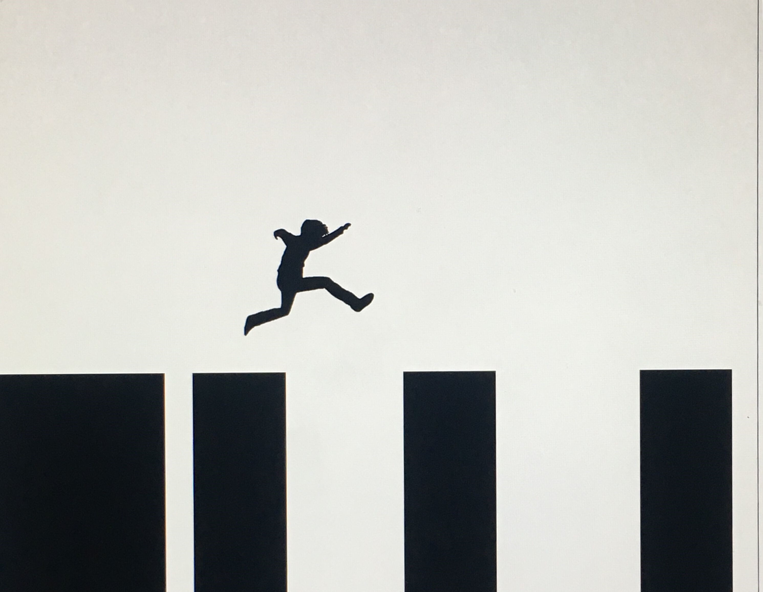 Een silhouet van een persoon die over zwarte lange balken springt.