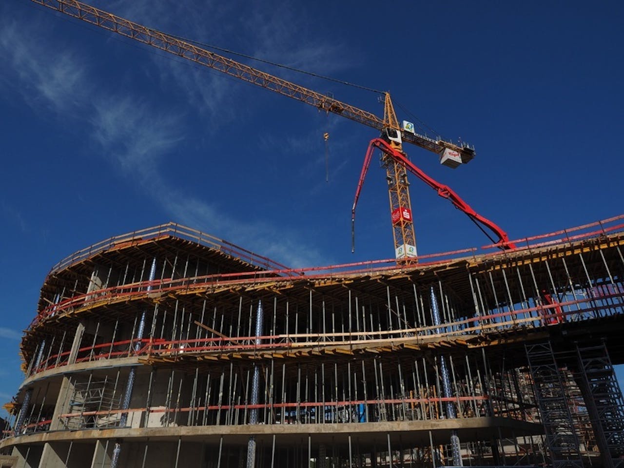 Twee kranen die een groot gebouw laten verrijzen.